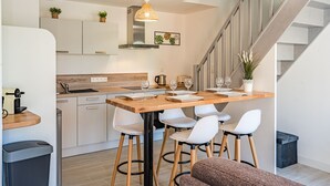 A modern kitchen with a wooden island, white bar stools, and a staircase leading to another level. - La Grange du Noé: Le Noé (Caen)