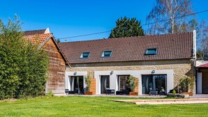A two-story building with a tiled roof, a wooden facade, and a small garden area with outdoor seating. - La Grange du Noé: Le Noé (Caen)