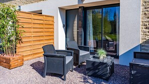 An outdoor seating area with wicker furniture, a wooden fence, and a large window. - La Grange du Noé: Le Noé (Caen)