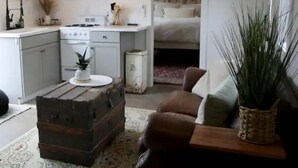 A compact living space with a kitchenette, a brown sofa, a wooden chest, and a potted plant. - Buckley Farm Casita (Menifee)