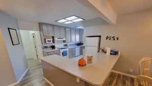 A modern kitchen with white cabinets, a central island, and a microwave above the stove. - Spacious Luxury Comforters of home while enjoying time away w/community pool :) (Roseville)