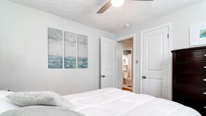 Un dormitorio con cama, paredes blancas y tres cuadros. Hay dos puertas, una que da al baño y otra a un armario.