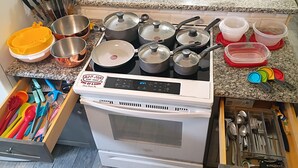 Uma cozinha com fogão, panelas, frigideiras e diversos utensílios.
