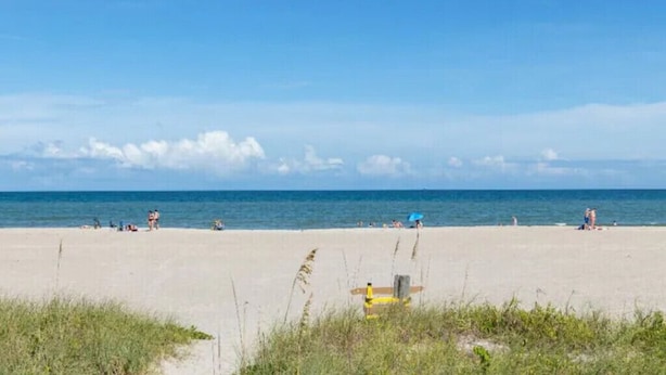 A beach with people sunbathing and swimming, a lifeguard chair, and a clear sky.