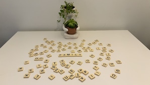 A table with scattered letter tiles spelling out "FAMILY" and a potted plant in the background.