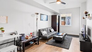 A modern living room with a grey sofa, a coffee table, a TV, and a gaming table.