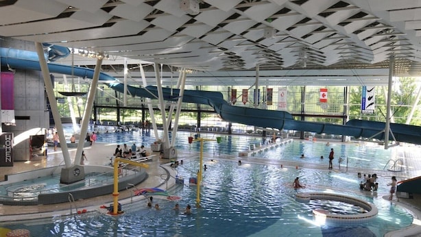 An indoor swimming pool with multiple lanes, slides, and a central water feature.
