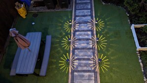 A patio area with a wooden deck, a seating arrangement, and a pathway with decorative lighting.