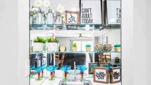 Een keuken met een glazen vitrine vol blauw glaswerk, een spoelbak en raamdecoratie met inspirerende citaten.
