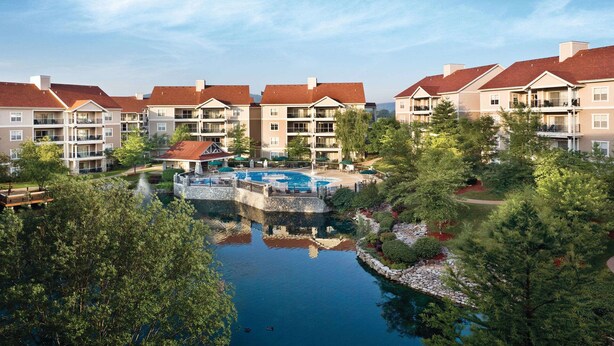 A resort with multiple-story buildings, a central swimming pool, and a landscaped area with trees and a small water feature. - 1BD Deluxe/Branson - Pools, Gym, BBQ, Game Room! (Branson)