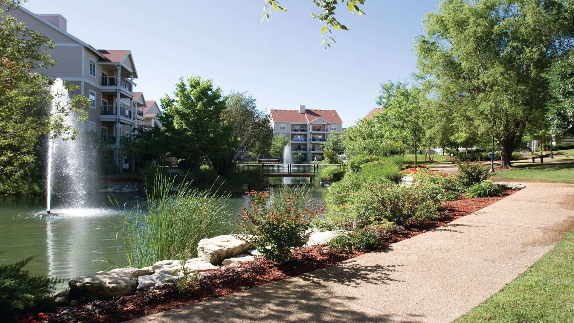 A tranquil outdoor setting with a pond, a fountain, and a walking path.