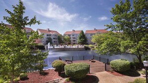 A lakeside view of a residential building with a wooden deck, a fountain, and a pool area. - 1BD Deluxe/Branson - Pools, Gym, BBQ, Game Room! (Branson)