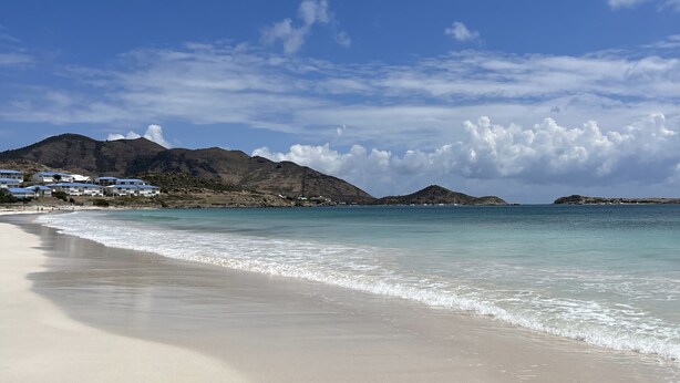 A beach with clear blue water, sandy shore, and distant mountains.