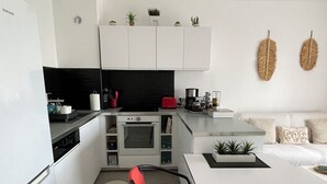 A modern kitchen with white cabinetry, a built-in oven, and a dining area with a white table and red chairs.