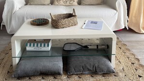 A living room with a white sofa, two decorative wall hangings, a woven basket, and a glass coffee table.