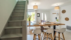 A dining area with a wooden table, four white chairs, and two pendant lights. - La Grange du Noé: L'Odon (Caen)