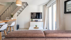 A modern living room with a sofa, a dining area with chairs, a TV, and a staircase. - La Grange du Noé: L'Odon (Caen)
