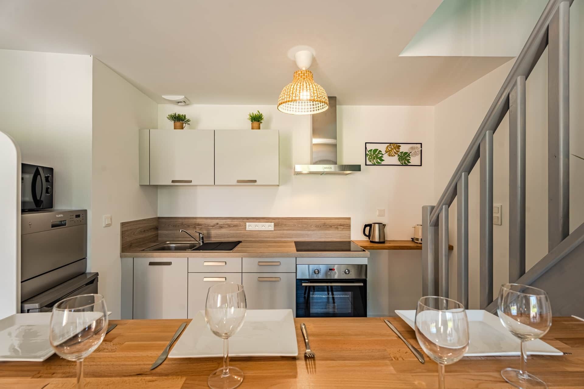 Une cuisine moderne dotée d’un plan de travail en bois, d’appareils électroménagers en acier inoxydable et d’un coin repas avec une table mise pour deux personnes.