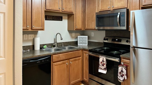 A kitchen with wooden cabinets, a stainless steel refrigerator, a microwave, an oven, and a dishwasher.