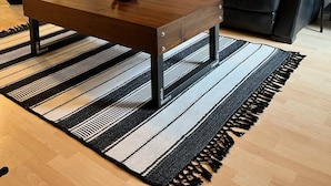 A living room with a black leather sofa, a wooden coffee table, and a striped rug.