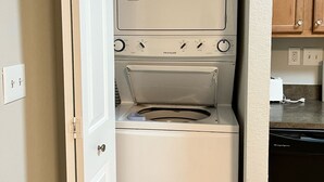 A compact laundry room with a front-loading washer and dryer, a white door, and wooden cabinets above.