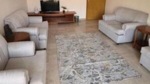 Un salon avec deux canapés, un téléviseur, un lustre et un tapis à motifs.
