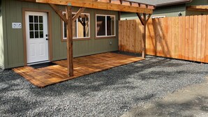 Un edificio pequeño de un piso con una terraza de madera y un patio cubierto.