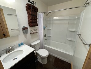 A bathroom with a white sink, toilet, and bathtub. There is a towel rack with brown towels and a metal shelf with toiletries.