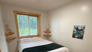 Un dormitorio con cama, ventana con persianas, un cuadro en la pared y una lámpara en el techo.