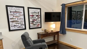 A cozy living room with a gray armchair, a wooden coffee table with a glass and coaster, a TV on a stand, and two framed fish species posters on the wall. - Soldotna Kenai Moose Lane Cottages # 3  Central to Kenai and Soldotna. (Soldotna)