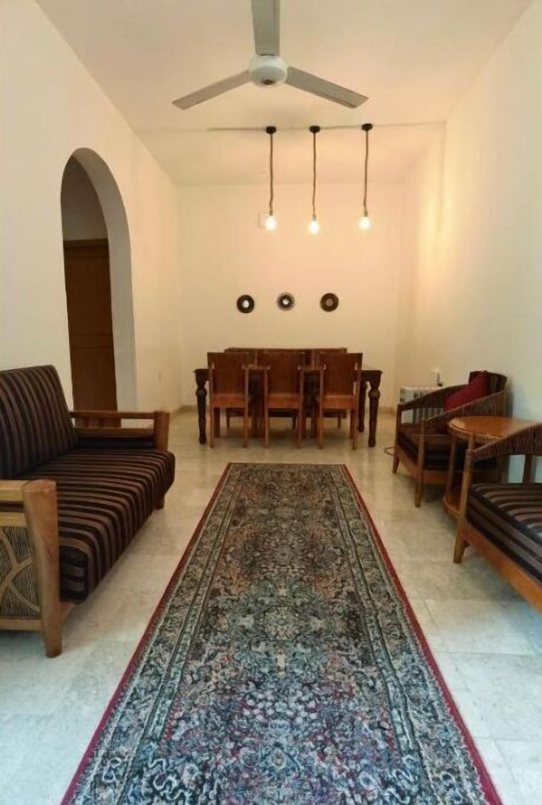 A living room with a sofa, dining table, chairs, a patterned rug, and a ceiling fan.