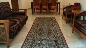 A living room with a sofa, dining table, chairs, a patterned rug, and a ceiling fan.