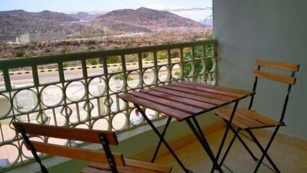 A balcony with a table and two chairs, overlooking a mountainous landscape. - Rummana Apartment 8 (Saiq)
