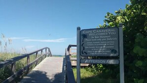 Een houten vlonder die leidt naar Cape Canaveral, met een bord waarop de regels voor het strand en Jefferson Ave staan.