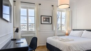 A hotel room with a bed, a desk, a chair, a lamp, a radiator, and a window with curtains. - Luxury San Niccolò in Florence by Mmega (Firenze)