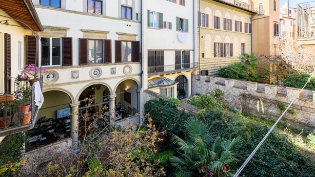 A courtyard with a stone wall, potted plants, and a balcony with a railing. - Luxury San Niccolò in Florence by Mmega (Firenze)