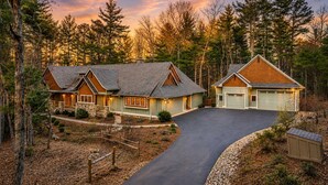 Une maison à deux étages avec un garage, entourée d’une zone boisée.