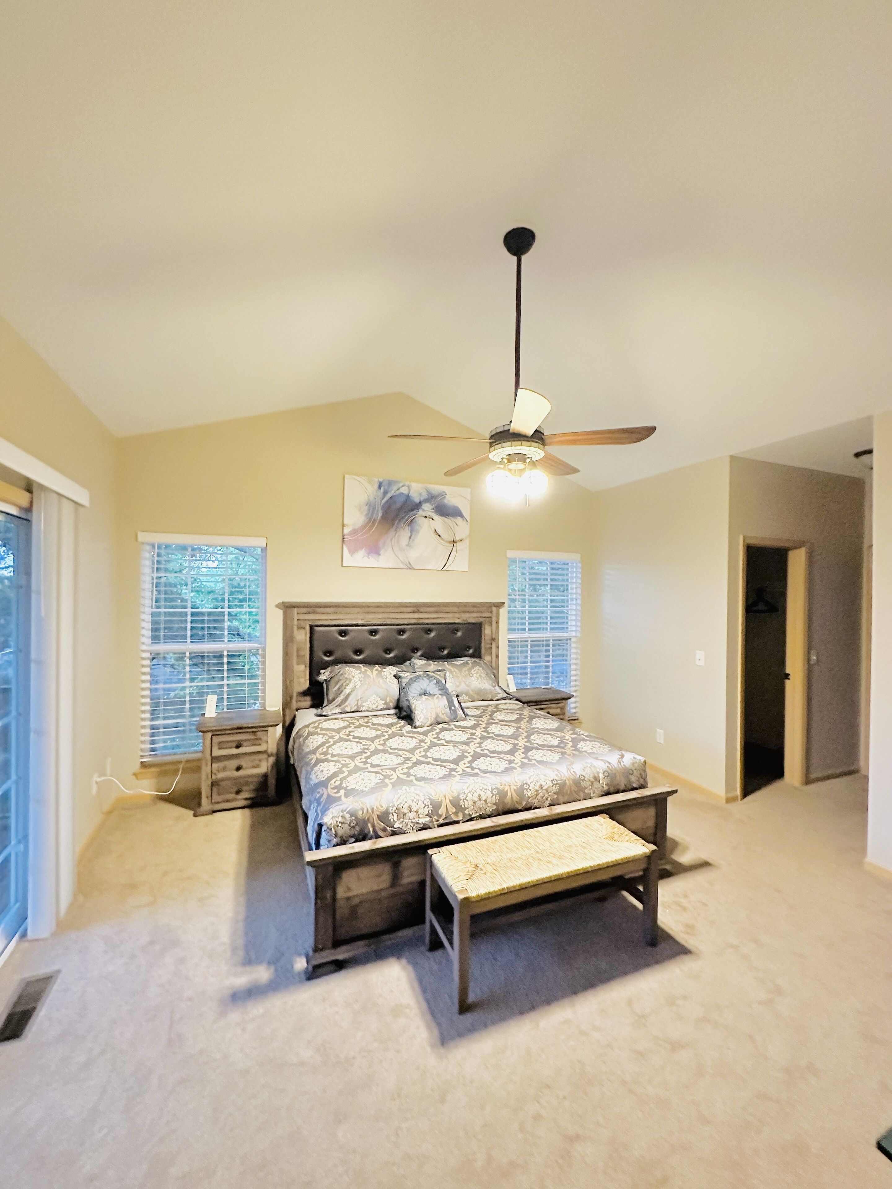 A bedroom with a bed, a ceiling fan, a nightstand, and a window with blinds.