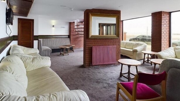 A hotel room with a large bed, a sofa, a small table, and a chair. There is a window with a view of the beach. - Jini Hotel (Blackpool)