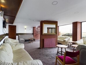 Habitación de hotel con una cama grande, un sofá, una mesita y una silla. Hay una ventana con vista a la playa.
