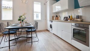 A modern kitchen with a dining area, featuring a washing machine, oven, and a table set for dining. - Loft L'Escale - 3 étoiles - Welkeys (La Ciotat)