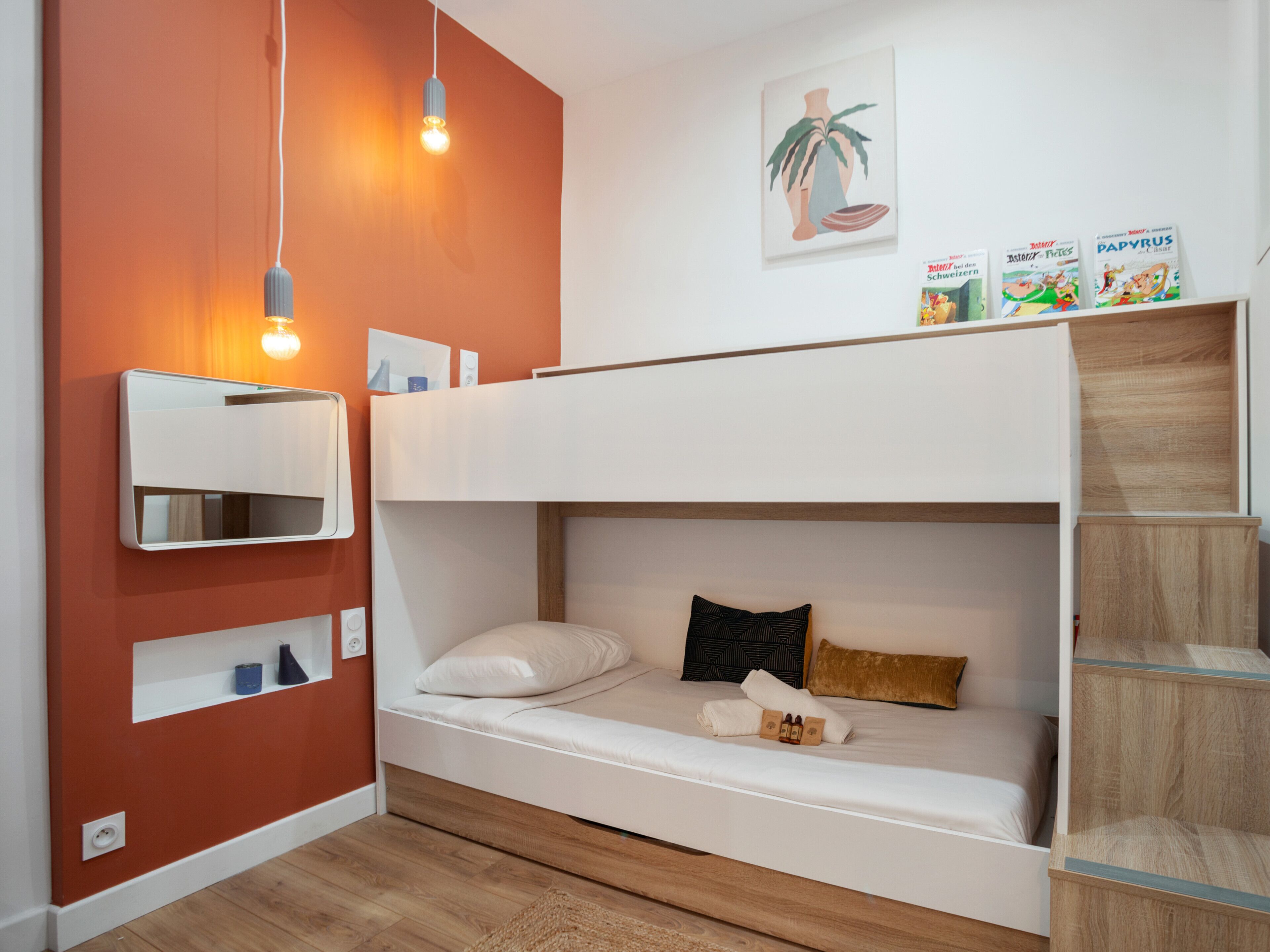 A bunk bed with a white headboard, a bedside table with a lamp, and a wall-mounted shelf.