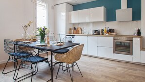 A modern kitchen with white cabinets, a wooden countertop, and a built-in oven. There is a dining area with a table and chairs, and a hanging light fixture above. - Loft L'Escale - 3 étoiles - Welkeys (La Ciotat)