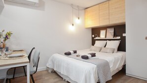 A bedroom with a bed, bedside table, chair, and a desk with a chair. - Suite Mugel - 3 étoiles - Welkeys (La Ciotat)