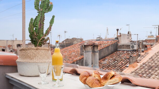 A rooftop terrace with a cactus, a bottle of orange juice, glasses, and a bowl of croissants. - Suite Mugel - 3 étoiles - Welkeys (La Ciotat)