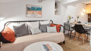 A modern living room with a striped sofa, a round coffee table, and a dining area with a wooden table and chairs. - Suite Mugel - 3 étoiles - Welkeys (La Ciotat)