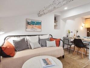 Ein modernes Wohnzimmer mit einem gestreiften Sofa, einem runden Couchtisch und einem Essbereich mit Holztisch und Stühlen.