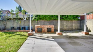 En overdækket terrasse med en murstenspejs, beton gulv og en hvid pergola.