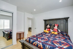 Een slaapkamer met een groot bed, twee zachte Mickey Mouse en Minnie Mouse knuffels, een houten hoofdbord en een spiegel.