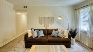 Uma sala de estar com um sofá marrom, um tapete estampado, um pendente de macramé e um abajur.